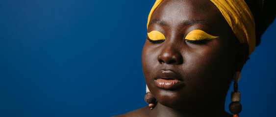 Close-up of gorgeous African woman with beautiful make-up and jewelry on blue background