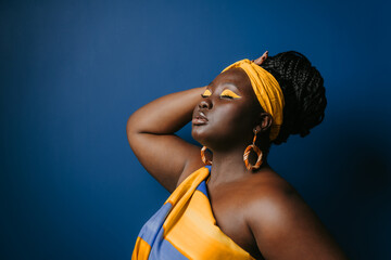 Attractive plus size African woman wearing traditional African attire and jewelry touching hair 