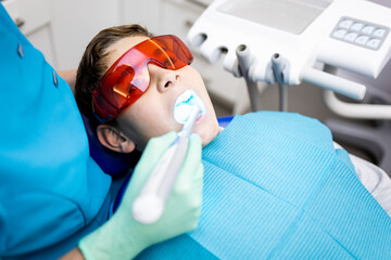 An unrecognizable dentist performs a dental filling on a child between 9 and 10 years old with a...