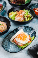 Flatbread with bacon and fried egg, salad with chicken fillet and rice with chicken on a table.