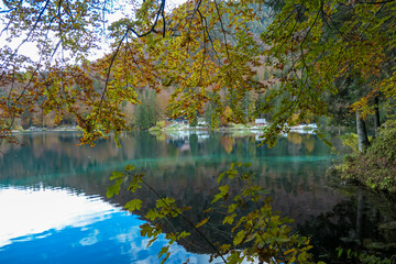 Panoramic view of Fusine Lake (Laghi di Fusine) in Tarvisio, Friuli-Venezia Giulia, Italy, Europe. Water reflection in clear green alpine lake. Autumn colored foliage. Calm serene tranquil atmosphere