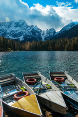 Colorful wooden boats on Fusine Lake (Laghi di Fusine) with scenic view of snow capped Julian...