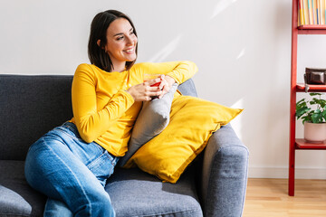 Happy young woman relaxing on couch while drinking tomato juice at home. Wellfare and healthy...