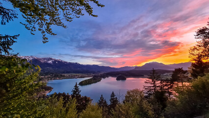 Panoramic sunset view on Lake Faak from Taborhoehe in Carinthia, Austria, Europe. Surrounded by high Austrian Alps mountains. Water surface reflecting soft sunlight. Remote alpine landscape in summer