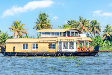 Indian traditional tourist houseboats floating on Pamba river, with palms at the coastline, Alappuzha, Kerala, South India