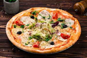 Pizza with cheese, chicken fillet, tomatoes, olives, lettuce and microgreens, traditional Italian food.