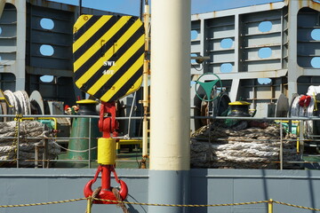 Steel red hook and black and yellow hoist block of ship's cargo crane secured by rope on main deck...