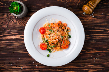 Pasta with shrimps, mussels, tomatoes, cheese and spices in a plate.