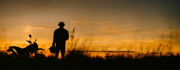 silhouette of a male motorcyclist at sunset and an off-road enduro cross-country motorcycle. - Powered by Adobe