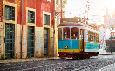 Lisbon Portugal. Vintage retro tram driving by street of paving stones in district Alfama. Cityscape panorama with old houses and tower sunny day