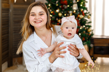 Cheerful mother and her cute  little girl daughter having fun and playing together near the Christmas tree