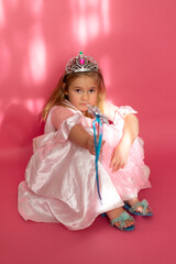 Selective focus view of cute little girl wearing princess dress and tiara while sitting on pink...