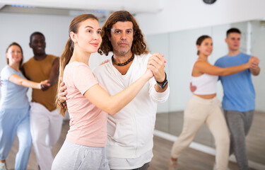 Smiling multiracial men and women enjoying partner dance while training together in modern studio