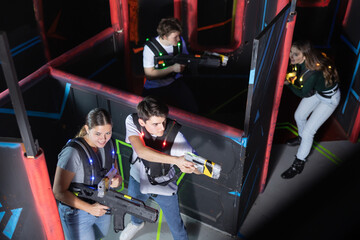 Four people having fun playing lasertag ducking behind cover in maze of lasertag arena
