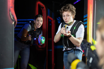 Two exciting players guy and woman with laser weapons in dark laser tag room