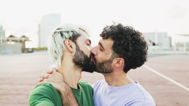 Young gay couple in love take a selfie kissing with smartphone. Handheld camera of a gay couple taking a selfie in real time while kissing at sunset. Valentine's Day