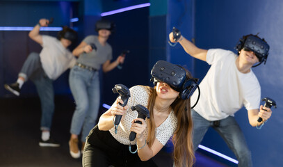Excited modern young woman with gaming controllers in hands and VR goggles having fun with friends...