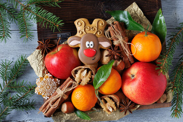 Christmas background card. A wooden box with gingerbread deer, cookies, apples, tangerines, nuts, walnuts, hazelnuts and fir branches on the table.