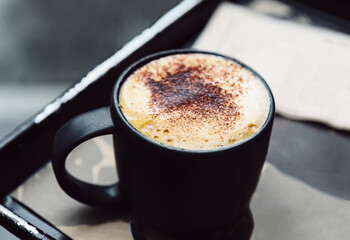 Cappuccino with cinnamon in a black cup on the table . Morning hot drink