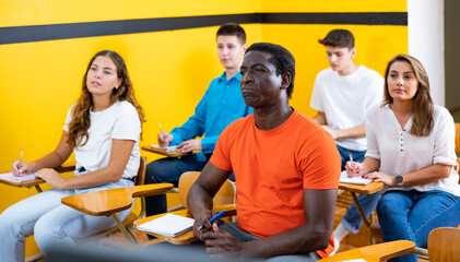 Group of multiracial people sitting at desks in classroom of school for taxi drivers.