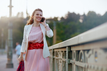 smiling female in dress and jacket in city talking on phone