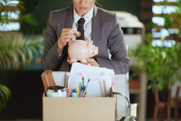 Modern woman worker in green office putting coin into piggy bank