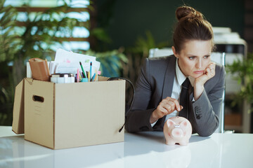 woman employee in green office putting coin into piggy bank