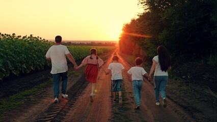 Dad, Mom, children run in summer at rural sunset. Large family walks through field of sunflowers, group of people runs in nature. Dad mom, daughter, son run hand in hand, family team. Parents and kids
