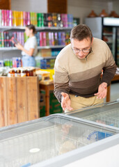 Man with glasses carefully selects frozen semi-finished products in a supermarket