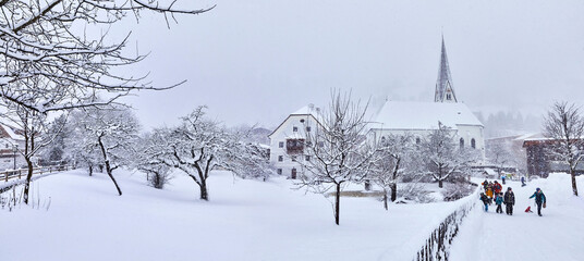 View of snowy Bramberg, with the village church and children playing, in Salzburger Land, Austria, - obrazy, fototapety, plakaty