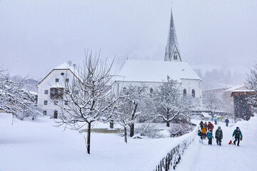 View of snowy Bramberg, with the village church and children playing, in Salzburger Land, Austria,