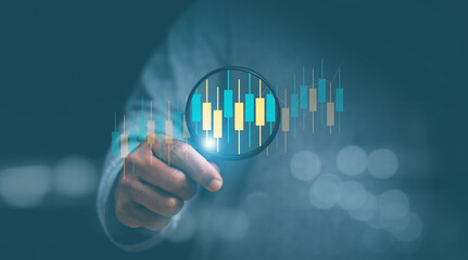 Finance and investment data search concept. Businessman hand holding magnifier and zooming at candlesticks bar chart of stock market data. Stock market analyzing, stock information search.