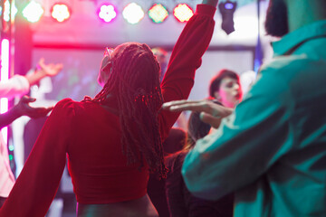 African american woman in red blouse jumping and dancing in crowded nighclub. Young clubbers having...