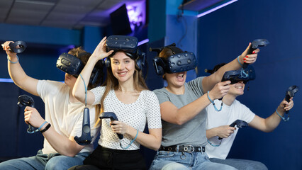 Cheerful emotional young woman in VR headset on head with joysticks in hands looking with excited...
