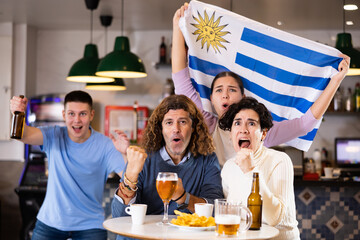 Fans with the flag of Uruguay celebrate the victory of their favorite team in a beer bar