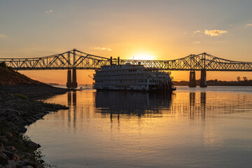 Fototapeta na wymiar A Paddle Wheeler Cruise Ship at Sunset in Front of the John R Junkin Drive Bridge over the Mississippi River in Natchez, Mississippi 