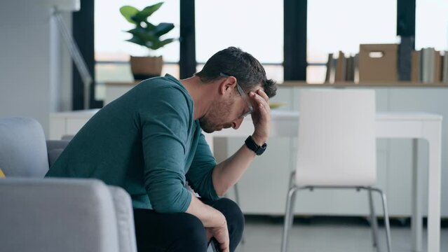 Video of worried mature man thinking about what he has read on his mobile phone while sitting on the couch at home