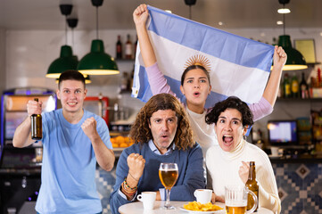 Happy sports supporters with flag of Argentina, rejoicing winning game with beer and snacks in pub