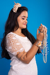 Beautiful, black-haired woman with shell tiara on her head holding and looking at pearl necklaces.