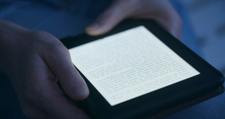 A woman reading an e-book in the evening or by night - 694577941