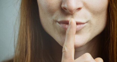 Woman gesturing to be quiet with a finger before her mouth.