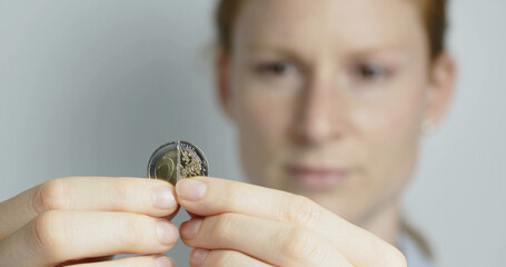 A young woman puts a broken 2 Euro coin together and smiles at the camera. - 694578156