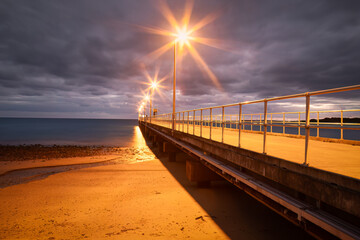 A jetty with lights on an overcast morning before sunrise in Mission Beach in tropical Queensland,...