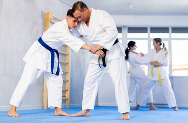 Practiced middle-aged and young male jujutsu practitioners demonstrating throw method in sports hall