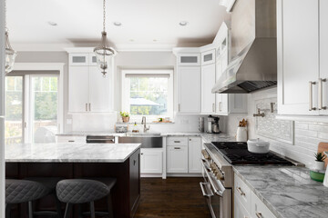 A white kitchen detail with pendant lights over a dark wood island, marble countertop, and a...