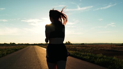 silhouette sports girl running along road sunset, runner athlete's leg, runner fitness sport, jumps...