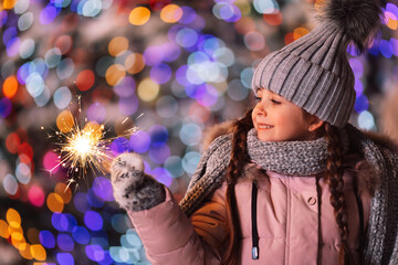 Charming little girl in knitted gray hat and winter pink jacket with sparklers and Christmas...