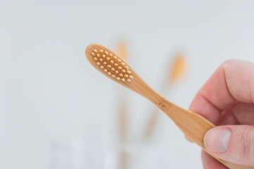  bamboo toothbrush.Teeth cleaning.Toothbrush in hand under tap water in bathroom. Hand takes a toothbrush from a transparent glass cup on the sink in a bright bathroom.Human hygiene concept 
