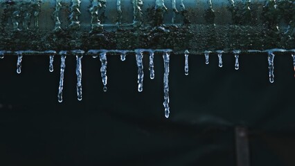 Water Drops Dripping from Tiny Icicles Melting on Edge of Roof Covered in Snow on Warm Winter Day