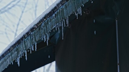 Water Drops Dripping from Tiny Icicles Melting on Edge of Roof Covered in Snow on Warm Winter Day